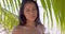 Enigmatic young woman at seashore amid green plants