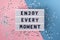 Enjoy every moment - text on display lightbox on blue and pink background