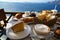 Enjoy island breakfast with beautiful Aegean sea view and morning sunlight including cappuccino cup, cake, baguette, croissant