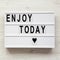 `Enjoy today` word on lightbox over white wooden background, from above. Top view, overhead, flat lay.