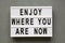 `Enjoy where you are now` words on modern board over grey background, top view. Flat lay, from above