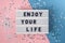 Enjoy your life - text on display lightbox on blue and pink background