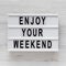 `Enjoy your weekend` words on a modern board on a white wooden surface, top view. Overhead, from above, flat lay. Close-up