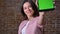 Enjoyable caucasian brunette girl with proud confident appearance showing green screen on tablet at camera straight