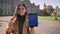 Enjoyable caucasian woman is standing and showing blue screen with happy smile and calm casual look, standing in urban