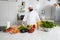 Enjoyable smiling chef with fresh vegetables on big table standing in the kitchen