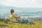 Enjoying the idyllic mountain landscape: Girl is sitting on idyllic meadow and enjoying the view over the far away city of