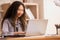 Enjoying the moment. At work, an Asian designer sits on a desk with his laptop, tablet, and documents, looking well and pleased