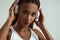 Enjoying music. Cute african woman adjusting headphones and looking at camera while standing against grey background