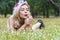 Enjoyment woman with flower on her hair blowing on dandelion flowers while lying on green grass in the park. Lovely girl