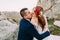 Enloved groom in stylish blue suit holding kissing his beautiful bride with cute head wreath on majestic mountain rocky