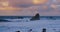 Enormous turbulent ocean waves crashing among huge rock formations at sunset. Slow motion. Colourful fluffy sky clouds