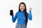 Enthusiastic korean woman shows mobile phone screen, looks excited and surprised, winning on smartphone, standing over