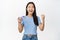 Enthusiastic smiling asian woman winning on mobile phone video game, looking satisfied and relieved, standing in t-shirt