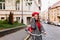 Enthusiastic woman in long tweed coat riding around old part of city with smile. Relaxed elegant girl in glasses posing