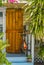 Entrance and porch to Key West House with rustic hurricane shutter by door and rusted bike parked surrounded by tropical greenery