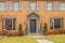 Entrance of stately upscale brick home with bay windows and grayish trim decorated for Christmas