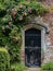 Entrance to a historic manor, framed by antique architectural elements and flanked by potted topiaries, features an aged door