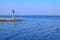 The entrance to a small harbor partitioned by a rope with red stripes. Small lighthouse in the background