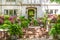 Entrance to up-scale chalet-like stucco house with brick stairs up to flower filled courtyard with fountain and trees reflected in