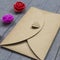 Envelope from craft paper with heart on it and three little roses flowers on wood background.