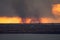 Environmental problem of fire on dry grass with smoke onthe horizon inflated by a strong wind during the sunset