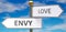 Envy and love as different choices in life - pictured as words Envy, love on road signs pointing at opposite ways to show that