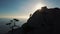 Epic Aerial view of a silhouette of a young woman climbing to the top of a mountain against the sea at sunset. Lady on