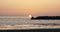 Epic background shot of sun rising over rippled sea with big stone wave breaker, a magnificent ocean sunrise panorama.