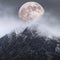 Epic digital composite image of Supermoon above mountain range giving very surreal fantasy look to the dramatic landscape image