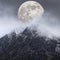 Epic digital composite image of Supermoon above mountain range giving very surreal fantasy look to the dramatic landscape image