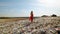 Epic dolly in: Young woman in red dress standing at huge trash dump with many seagulls in background