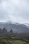 Epic dramatic landscape image of view from Elterwater across towards Langdale Pikes mountain range on foggy Winter morning