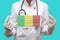 Epidemic in Bahamas. Young woman doctor in a medical coat or suit and gloves holds a medical mask with the print of the flag of