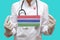 Epidemic in Gambia. Young woman doctor in a medical coat or suit and gloves holds a medical mask with the print of the flag of