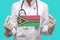 Epidemic in Vanuatu. Young woman doctor in a medical coat or suit and gloves holds a medical mask with the print of the flag of