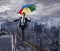 Equilibrist businessman walk on a rope with umbrella over the city. Concept of overcome the problems and positivity