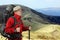 Equipped with traveler in a red jacket with Hiking poles looks into the distance