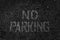 Eroded no parking sign painted in white on dark asphalt