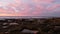 Eroded tide pool rock formation in California. Sunset sky reflection in water.