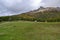 Esplanade with green grass, a forest below and mountains in the background on a cloudy autumn day