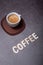 Espresso coffee served on a white cup with coffee wooden letters written on a grey textured board