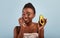 Essential oils for skincare. Pretty black woman holding ripe fresh avocado half, standing over blue background