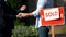 Estate agent and man exchanging money and house keys against sold signboard