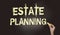 Estate planning words in pale yellow on blackboard and hand with chalk. Real estate business rent and sales concept