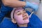 An esthetician applies clay facial mask to a customer\'s face prior to using a phototherapy device at an aesthetic clinic