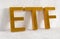 ETF - exchange traded funds - acronym in golden letters leaning against concrete wall on white wooden floor background