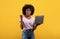Euphoric black lady celebrating success with laptop, raising clenched fist over yellow background