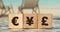 Euro, yen and pound signs on wooden cubes on ocean beach landscape background. Diferent money currency signs, profit concept