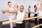 European female ballet teacher showing moves in front of a group of multiracial ..dancers in large dancing studio